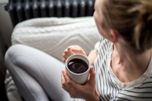 A young woman who is enjoying a cup of coffee while relaxing on a sofa. Conveys warmth and comfort in a relaxing environment.