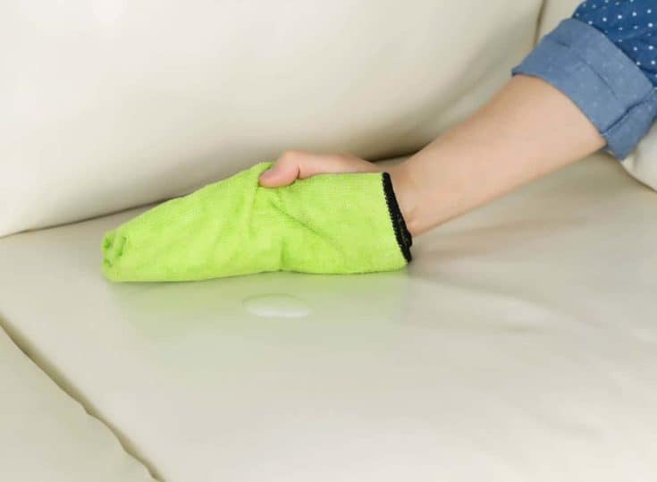 A person quickly blotting a spill on a leather couch with a dry cloth to prevent stains.