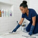 Professional house cleaner scrubbing bathroom tiles during deep cleaning service